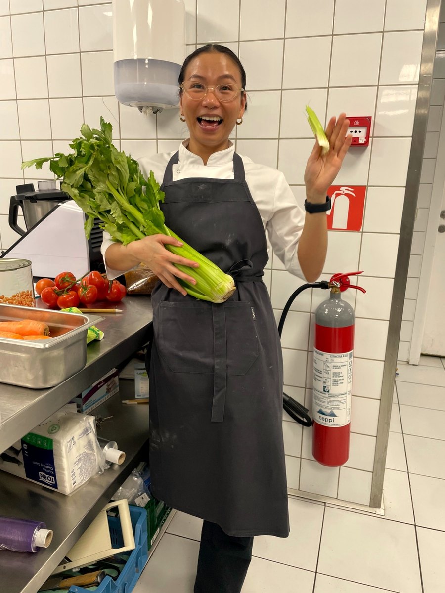 Rein Estebal in chef whites at the prep station, laughing, celery in her arm.